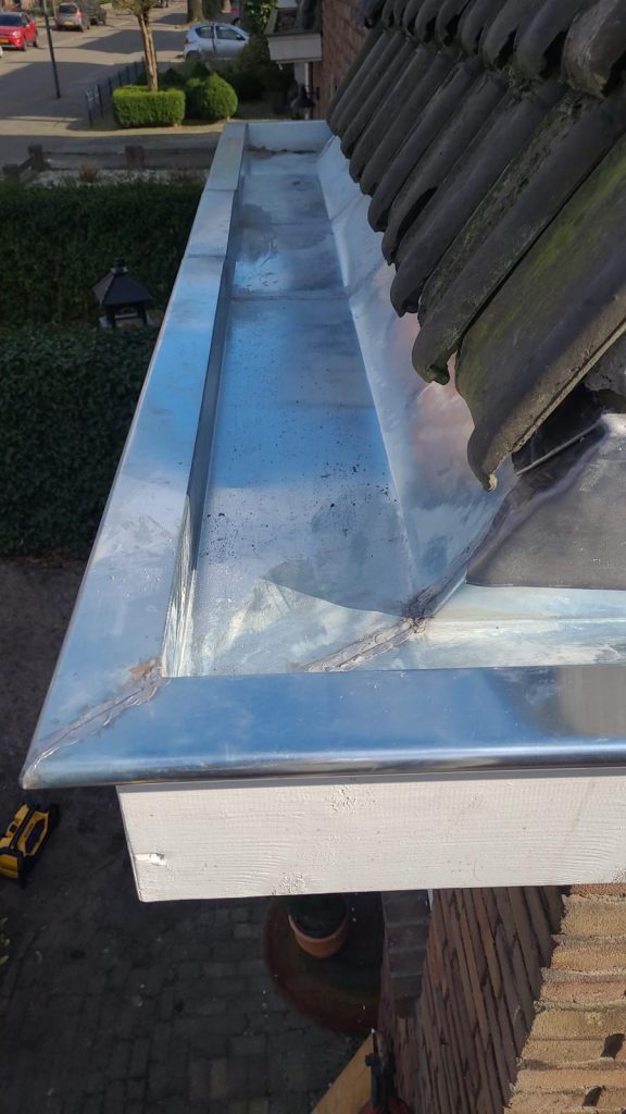 Nieuwe zinken dakgoot langs een pannendak